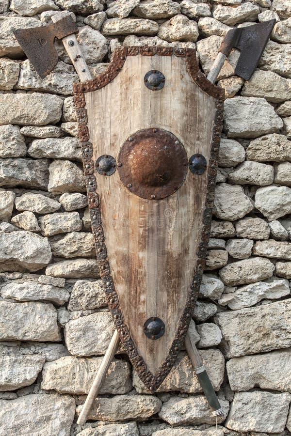 Ancient weapons on a stone wall. Wooden shield with iron accents royalty free stock image