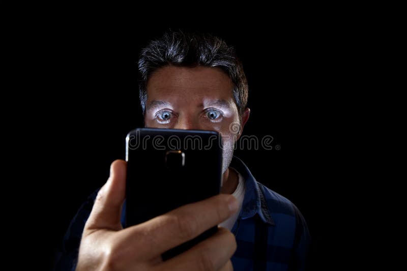 Close up portrait of young man looking intensively to mobile phone screen with blue eyes wide open isolated on black background. Close up portrait of young man royalty free stock image