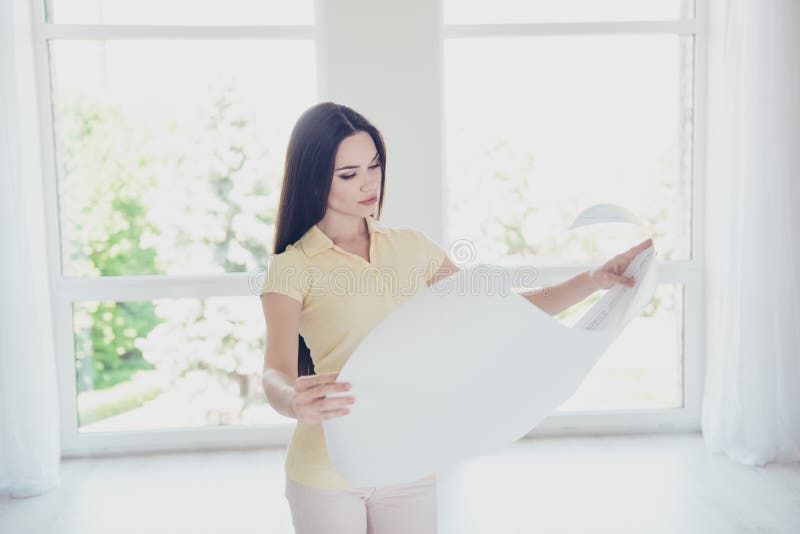 Focused young pretty designer is looking at the scheme of the pr. Oject, she is in a casual outfit, with long hair, standing in light room royalty free stock images