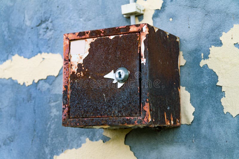 The old electric shield hangs on the exfoliating wall of the house, a rusty metal box hanging on the wall. The old electric shield hangs on the exfoliating wall royalty free stock images