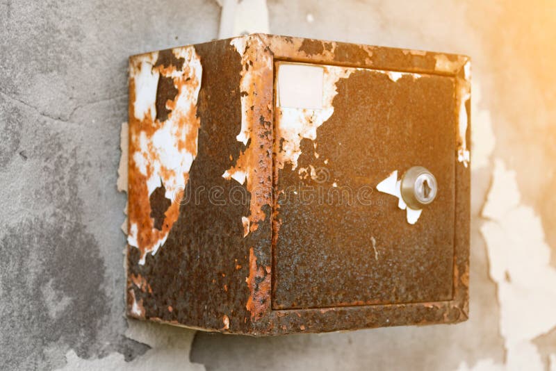 The old electric shield hangs on the exfoliating wall of the house, a rusty metal box hanging on the wall. The old electric shield hangs on the exfoliating wall stock photo