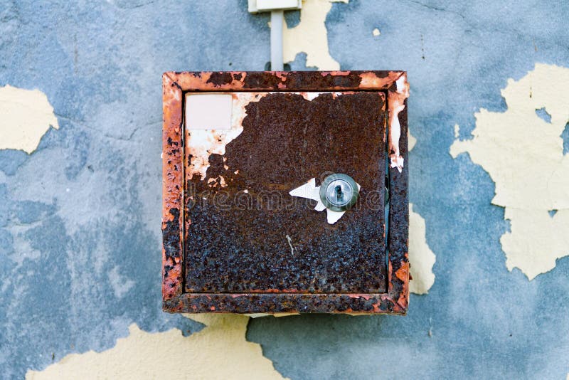 The old electric shield hangs on the exfoliating wall of the house, a rusty metal box hanging on the wall. The old electric shield hangs on the exfoliating wall royalty free stock photos