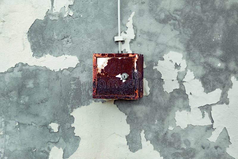 The old electric shield hangs on the exfoliating wall of the house, a rusty metal box hanging on the wall. The old electric shield hangs on the exfoliating wall royalty free stock images