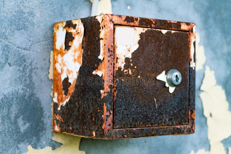 The old electric shield hangs on the exfoliating wall of the house, a rusty metal box hanging on the wall. The old electric shield hangs on the exfoliating wall stock image