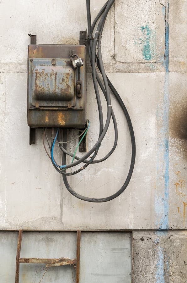 Old rusty unkempt electric shield with a switch. On the wall of an industrial building made of concrete blocks with molten wires stock photo