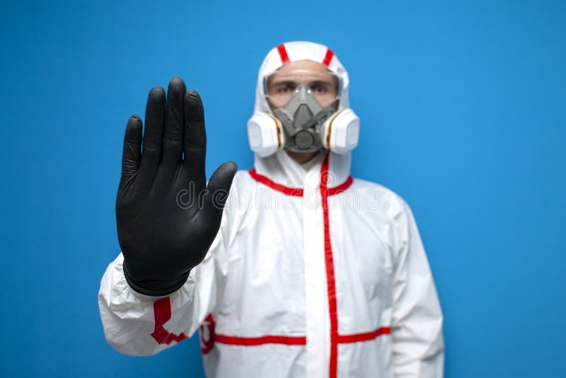 Resistance to coronavirus. disinfection worker in protective equipment and respirator shows a stop sign, virologist on blue. Isolated background royalty free stock photography