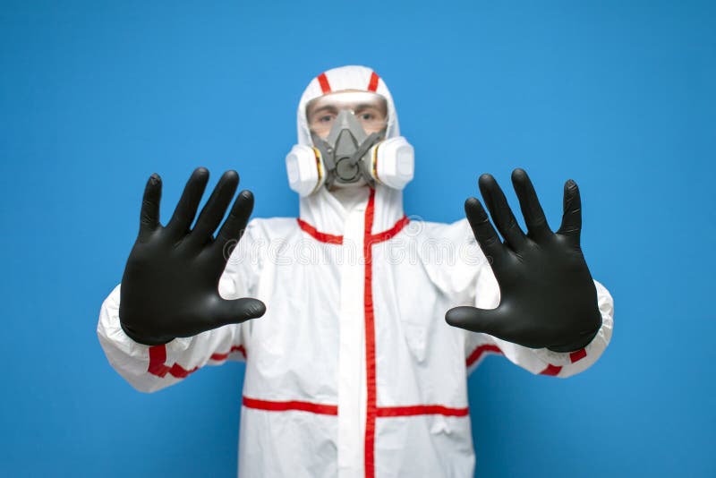 Resistance to coronavirus. disinfection worker in protective equipment and respirator shows a stop sign, virologist on blue. Isolated background stock photo