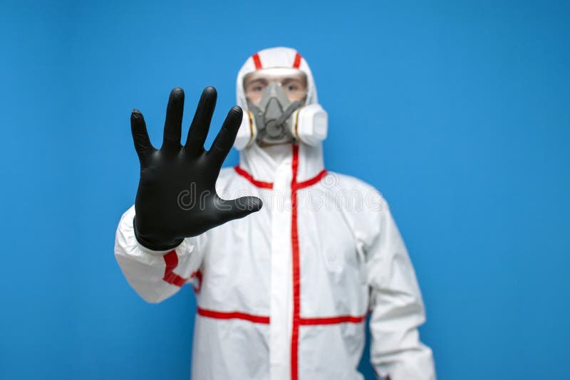 Resistance to coronavirus. disinfection worker in protective equipment and respirator shows a stop sign, virologist on blue. Isolated background royalty free stock image