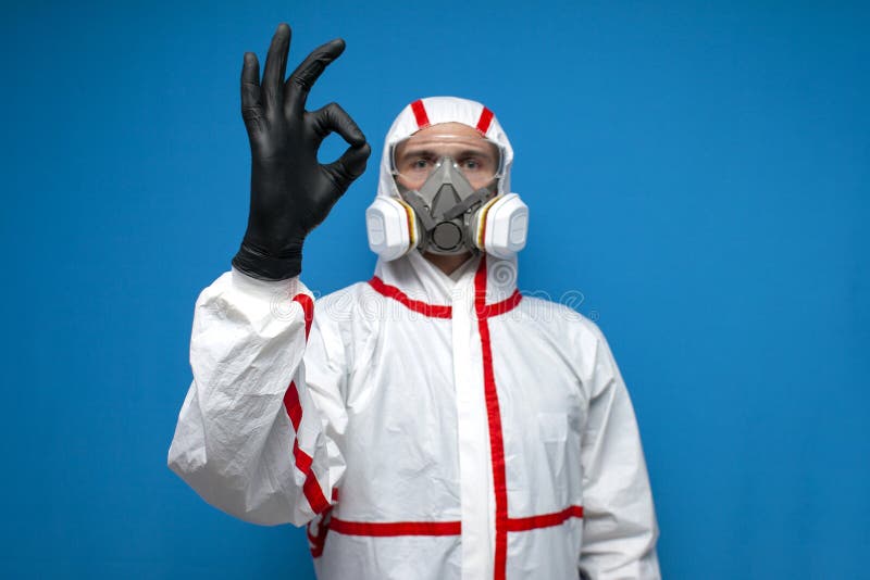 Resistance to coronavirus. disinfection worker in protective suit and respirator shows ok sign, virologist on blue background. Resistance to coronavirus stock photography