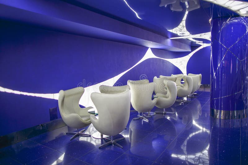 Interior in white-blue color scheme, with armchairs and tables. White rotating chairs and glass tables in a blue room with modern lighting. Interior in white and royalty free stock photos