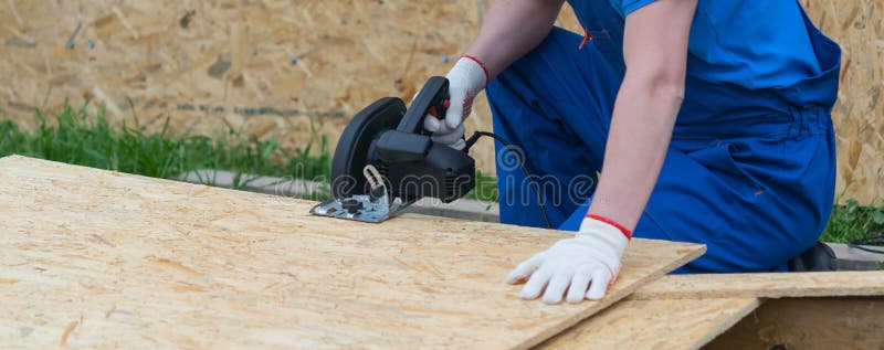 A worker in a blue uniform and protective gloves, cuts a wooden shield with an electric saw, close-up stock photos