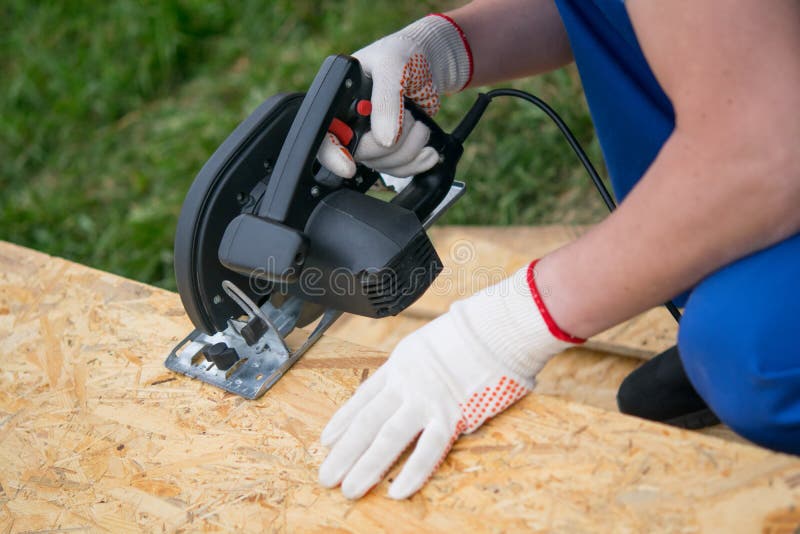 Worker in protective gloves, cuts a wooden shield, electric saw, close-up stock photo